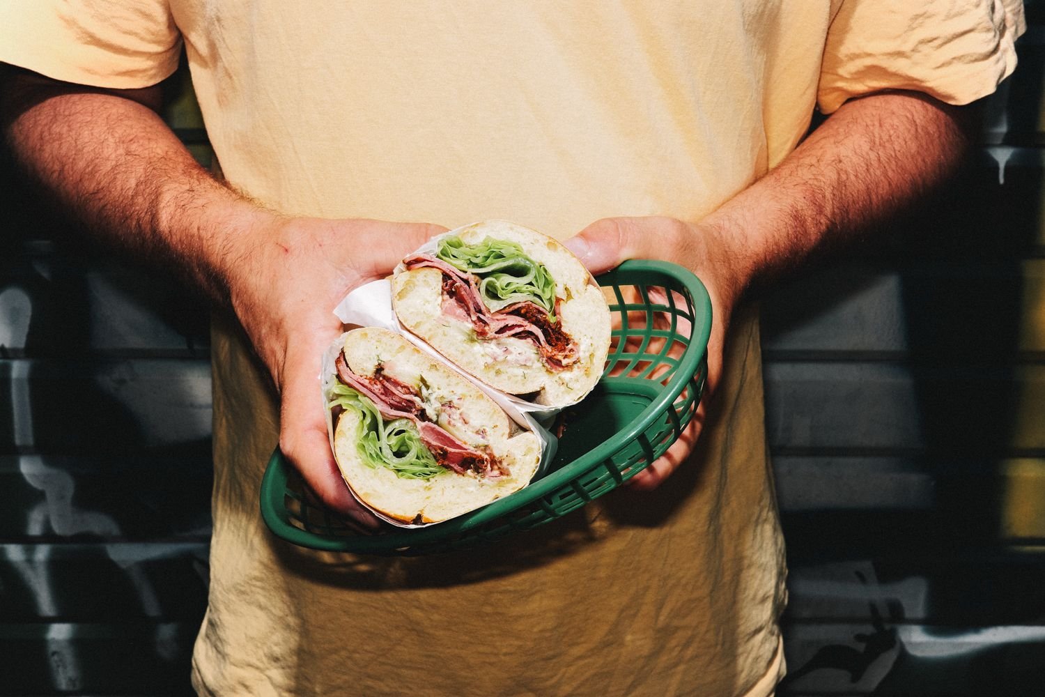 Sandwich pastrami LABC coupé en deux, tenu à deux mains dans un panier