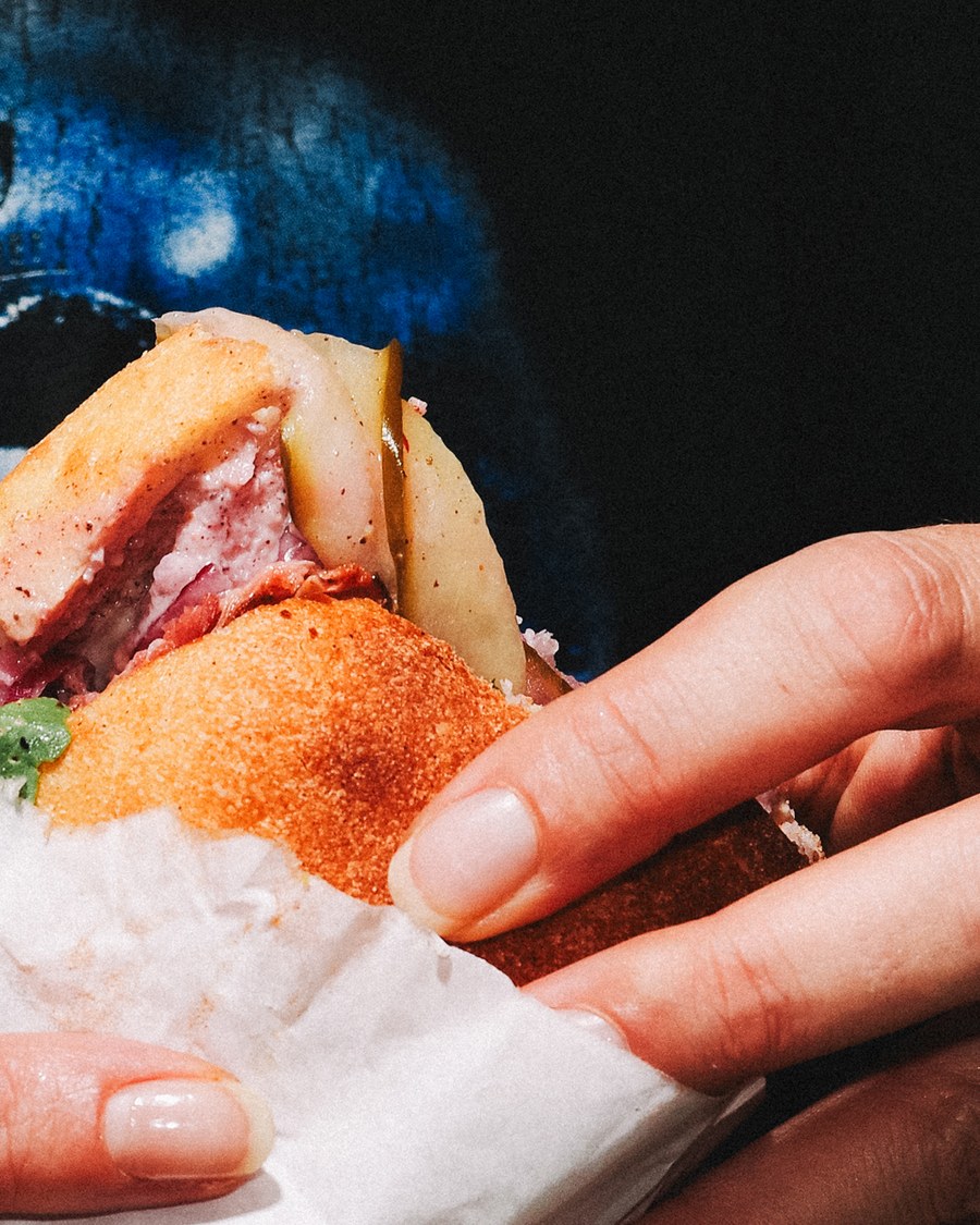 Sandwich pastrami LABC tenu à la main, emballé dans du papier